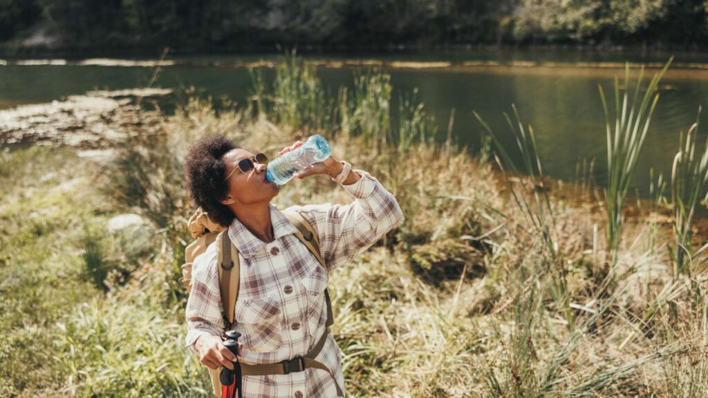 Woman Drinking Water While Hiking On Mountain
