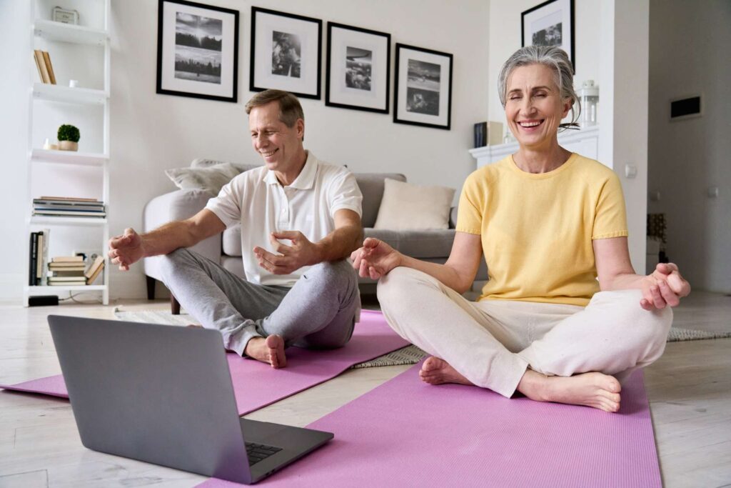 Happy relaxed couple having fun meditating together at home with laptop