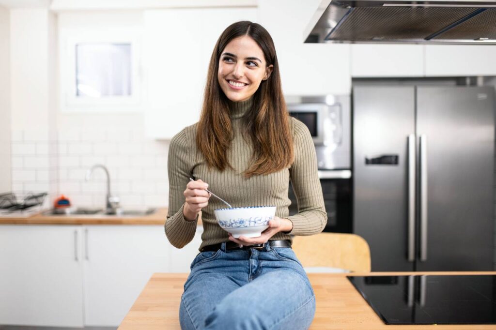 Healthy Snacking Tips - woman with a bowl and spoon smiling at kitchen healty food